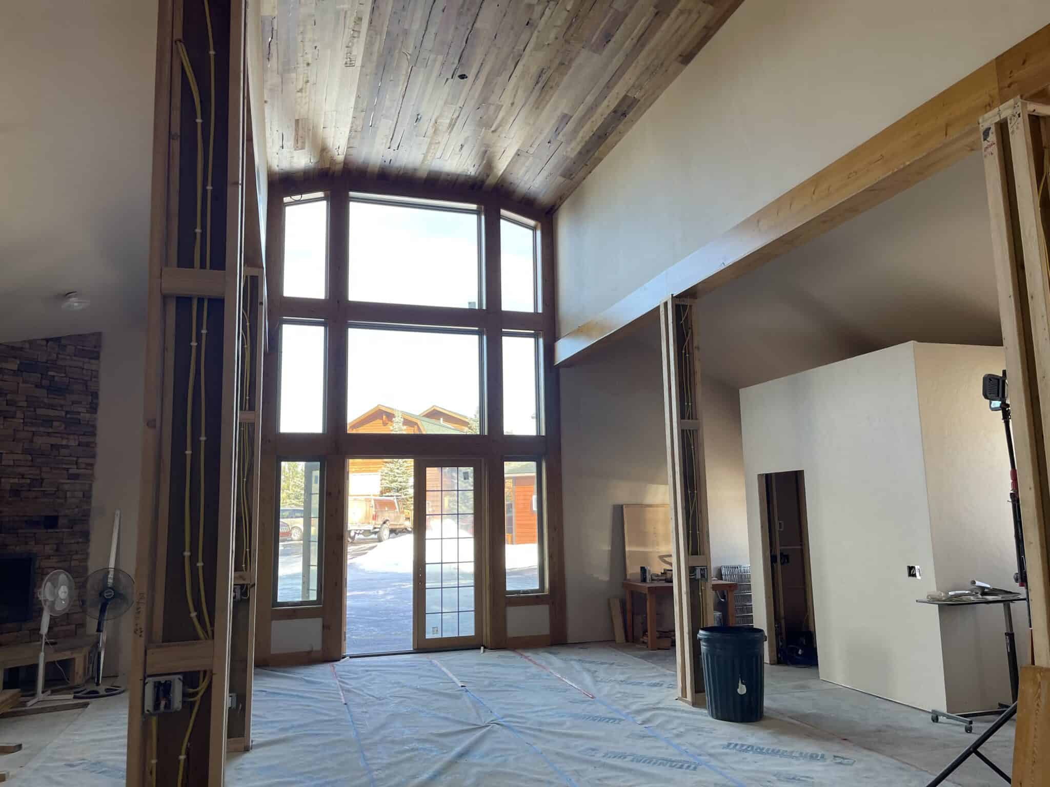 Spacious room with large windows and high wooden ceiling under construction.
